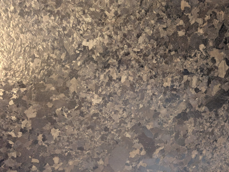 Nahaufnahme einer satinierten Natursteinoberfläche mit matter, haptischer Textur und dezentem Seidenglanz.